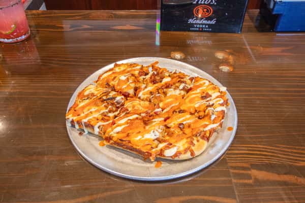 Buffalo chicken pizza topped with melted cheese, drizzle sauce, and crispy chicken pieces on a metal tray at a brewery restaurant