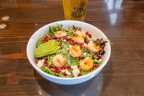 Fresh shrimp and avocado salad with mixed greens, pomegranate seeds, and crumbled cheese served with a craft beer at a brewery