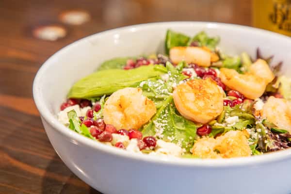 Fresh mixed green salad topped with seared scallops, pomegranate seeds, and grated cheese in a white bowl at a restaurant