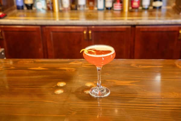 Craft cocktail in a coupe glass with citrus garnish served on a polished wooden bar ChipotleBlueBurgerHeadon.jpg