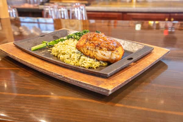 Grilled salmon filet glazed and served on a sizzling skillet with herb rice and broccolini at a restaurant