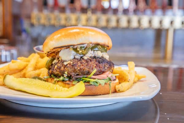 Gourmet burger with blue cheese and chipotle flavors served with fries and pickle on a bar top