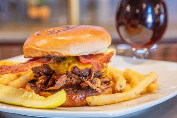 BBQ bacon cheeseburger with crispy onion straws and melted cheddar on a toasted brioche bun, served with seasoned fries and a pickle at a brewery bar