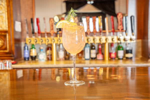 Refreshing cocktail with citrus garnish served in front of a row of beer taps at a bar