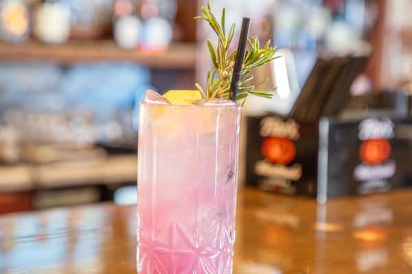 Pink citrus cocktail with rosemary garnish and lemon served in a tall glass at a craft brewery bar