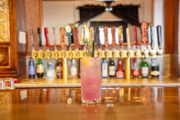 Craft cocktail with rosemary garnish served in a tall glass on a polished bar with beer taps in the background