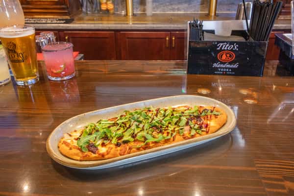 Mediterranean-style flatbread pizza topped with fresh herbs, diced vegetables, and cheese served on a wooden board at a brewery bar