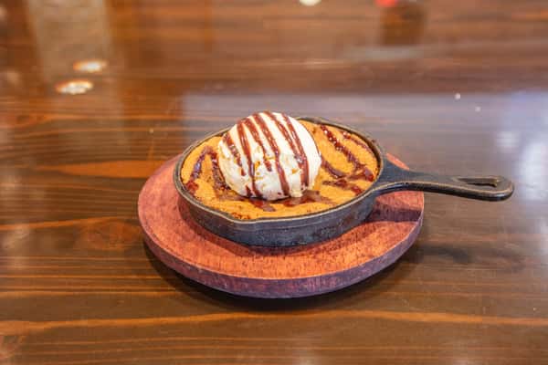 Warm skillet chocolate chip cookie topped with vanilla ice cream and chocolate drizzle served on a wooden board at a restaurant