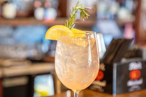 Close-up of a citrus cocktail with lemon slice and rosemary garnish over ice at a stylish bar setting