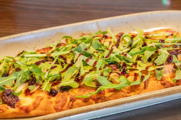 Mediterranean-style flatbread pizza topped with fresh herbs and vegetables on a bar table