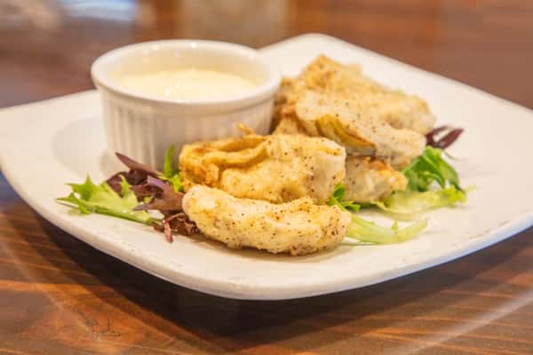 Fried artichoke hearts served over mixed greens with dipping sauce on a white plate at a casual restaurant
