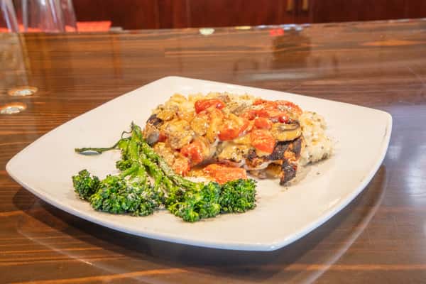 Chicken marsala with mushrooms and creamy sauce served over rice with broccolini on a white plate at a casual upscale restaurant