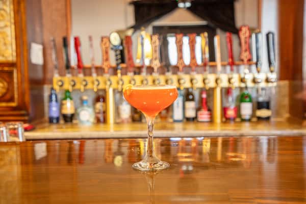 Pink craft cocktail in a coupe glass with citrus garnish served at a brewery bar with tap handles behind
