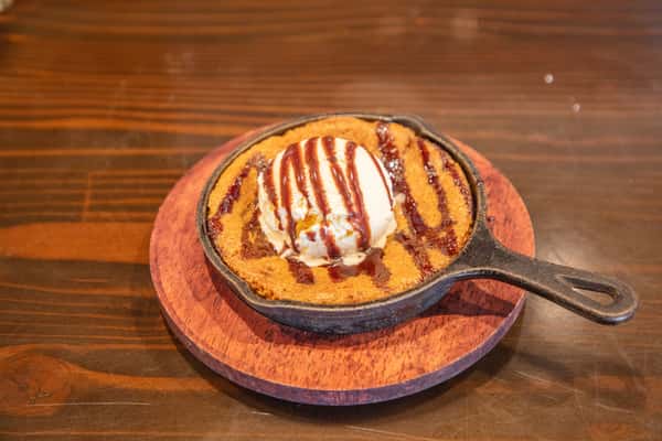 Warm skillet chocolate chip cookie dessert topped with ice cream and chocolate drizzle