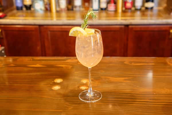 Sparkling citrus cocktail with lemon garnish and rosemary sprig served in a stemmed glass on a polished brewery bar