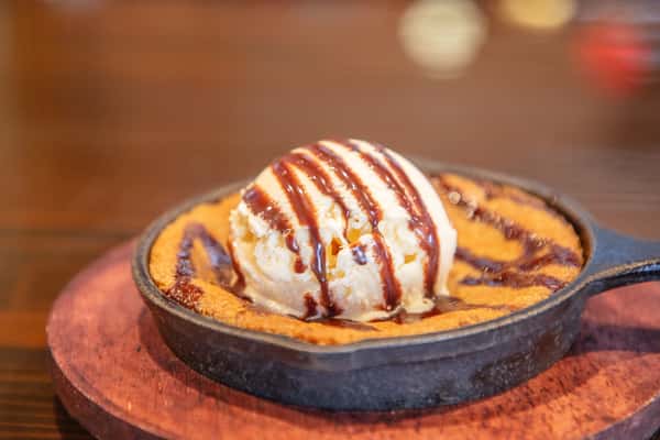 Warm skillet chocolate chip cookie topped with vanilla ice cream and chocolate drizzle served in a cast iron pan