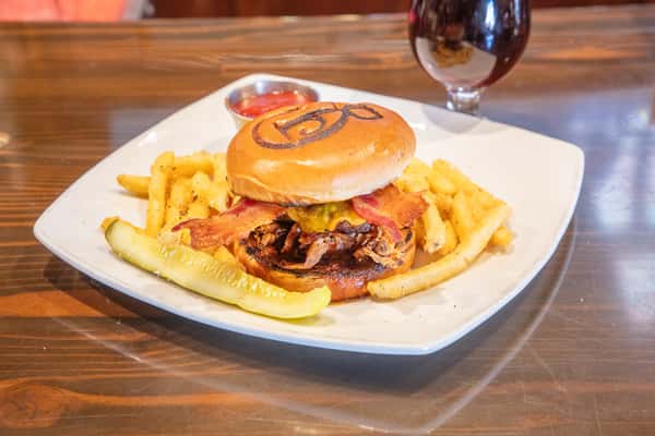 BBQ bacon cheeseburger with crispy onion straws and melted cheddar on a branded bun, served with seasoned fries and a pickle alongside a craft beer at a brewery restaurant