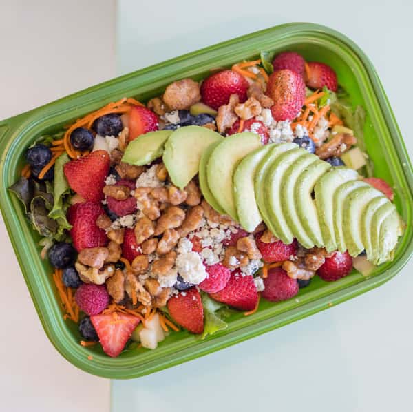 Summer Salad made with mixed greens, shredded carrots, strawberries, blueberries, raspberries, blue cheese crumbles, candied walnuts, sliced avocado, and served with raspberry vinaigrette.