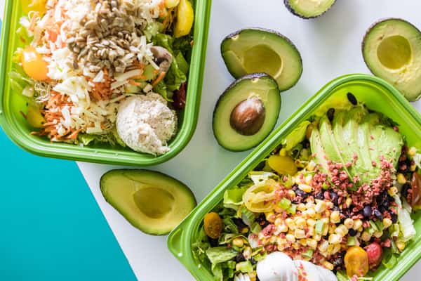 The Jan's Classic Salad and a Santa Fe Cobb Salad surrounded by avocados cut in half.