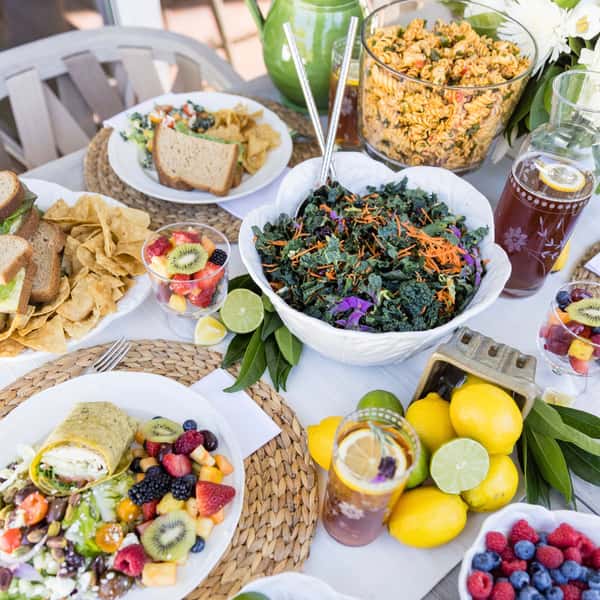 A spread of catering menu items from Jan's Health Bar including wraps, sandwiches, kale salad, pasta salad, and fruit.