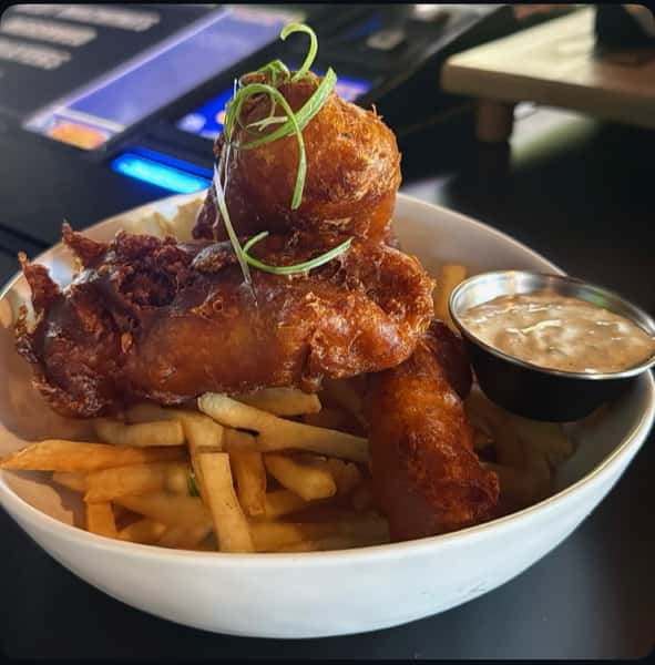 Golden fried chicken tenders over fries, garnished with green onions, with a side of dipping sauce