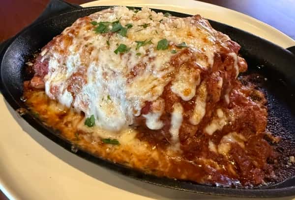 Baked lasagna smothered in melted mozzarella and marinara sauce, garnished with fresh herbs, in a cast-iron skillet