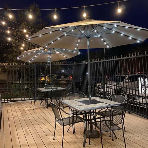 Outdoor restaurant patio at night with metal tables, chairs, illuminated umbrellas, and string lights.