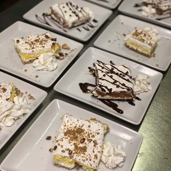 Assorted slices of layered cream desserts plated with whipped cream, crumbs, and chocolate drizzle.