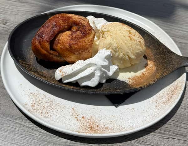 Warm cinnamon roll dessert served in a skillet with vanilla ice cream and whipped cream