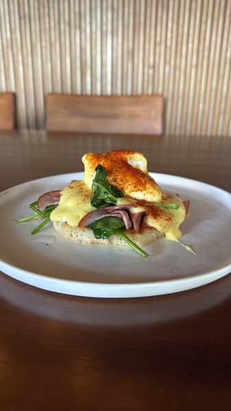 Eggs Benedict with ham and spinach on an English muffin, topped with hollandaise sauce