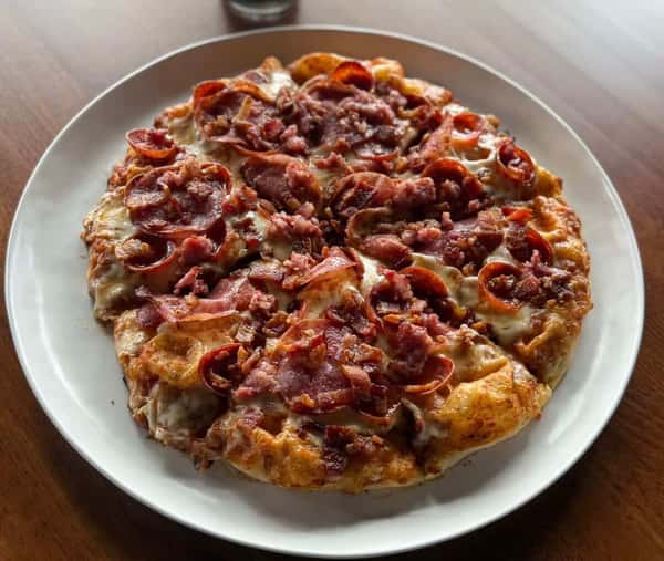Thin-crust pizza loaded with crumbled bacon and melted cheese, served on a white plate