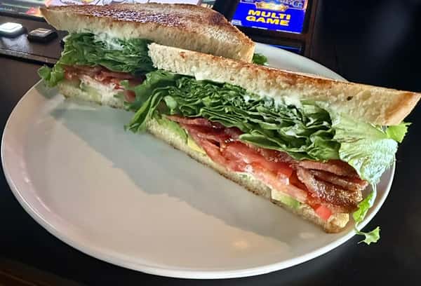 Toasted sandwich cut in half and stacked with fresh greens, tomato, and bacon, served on a white plate