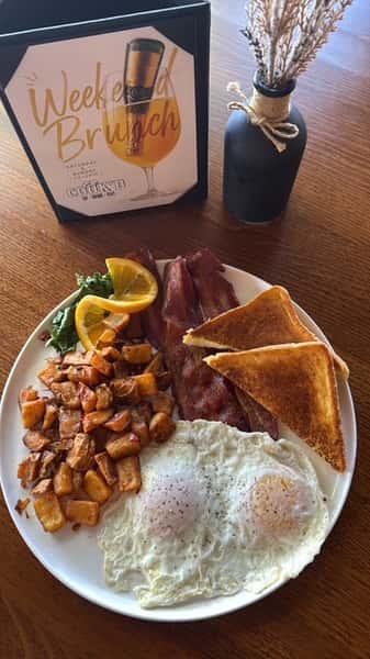 Breakfast plate with two eggs, crispy bacon, seasoned breakfast potatoes, and buttered toast