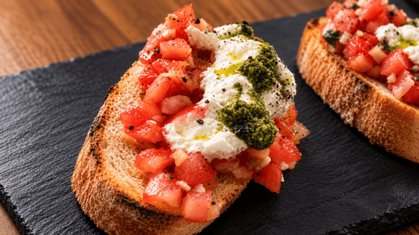 Close-up of bruschetta on toasted bread topped with diced tomatoes, fresh mozzarella, and basil pesto