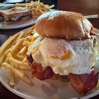 A bacon cheeseburger topped with a fried egg, served with thin-cut fries.