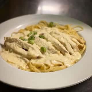 Fettuccine in a creamy Alfredo sauce topped with sliced chicken and green onions.