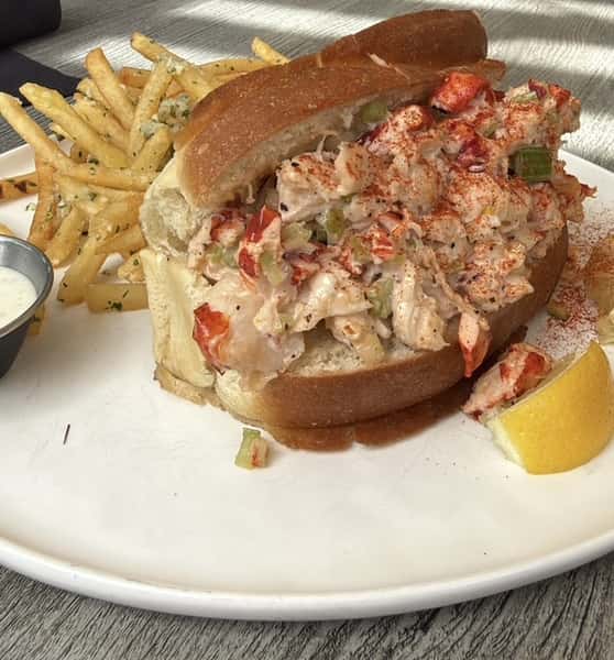 Lobster roll piled high on a toasted bun, served with fries and a lemon wedge
