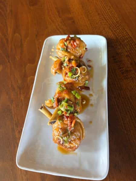 Row of bite-sized appetizers topped with colorful diced vegetables and herbs on a long white plate