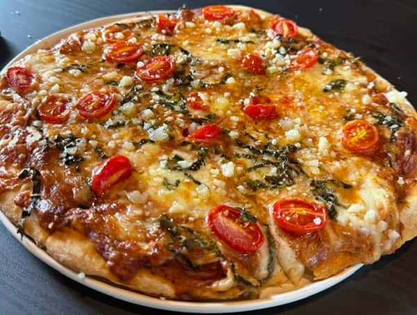 Thin-crust pizza topped with cherry tomatoes, fresh basil, and crumbled cheese