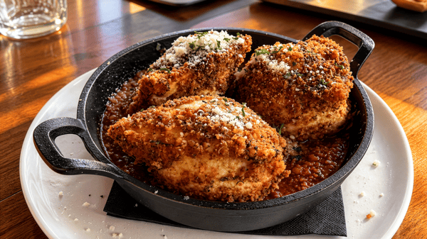 Baked ravioli with a golden, crispy breaded crust, garnished with fresh herbs and served in a cast-iron skillet