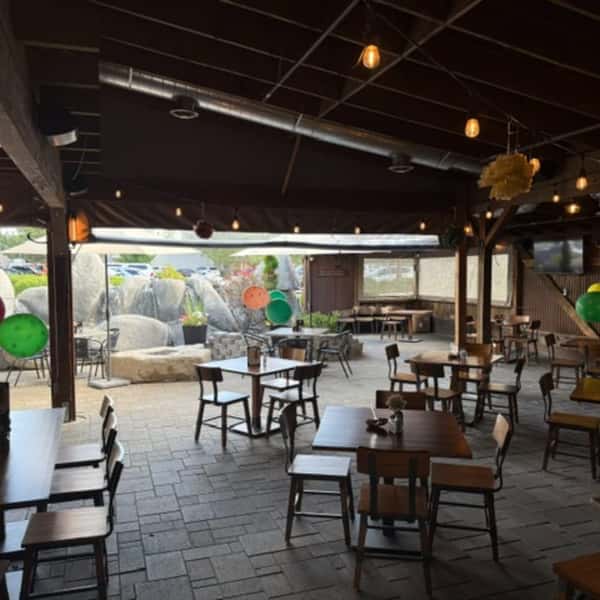 Spacious covered restaurant patio with tables, exposed beams, hanging lights, televisions, and an adjacent outdoor area.