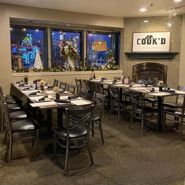 Cook'd dining room decorated for the holidays, with set tables, a fireplace, and festive window displays.