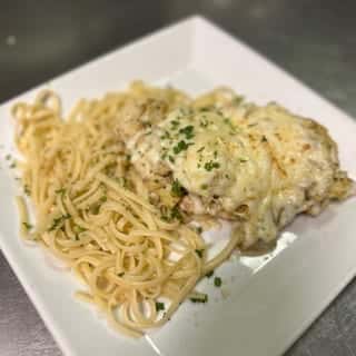 A cheese-topped chicken entrée served with creamy herb pasta on a square white plate.