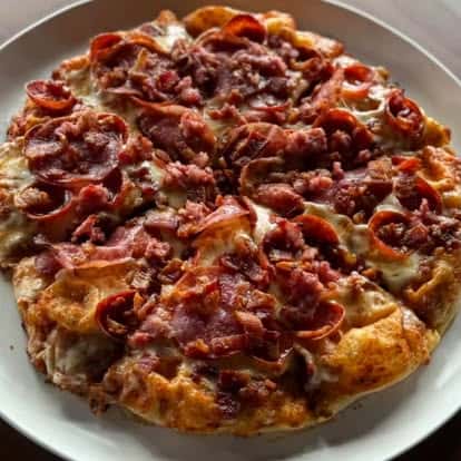 A thick-crust pizza loaded with melted cheese, pepperoni, bacon, and other meats.
