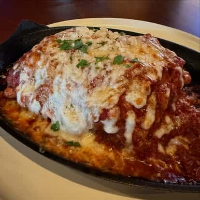 A baked Italian entrée covered in marinara sauce and melted cheese, served sizzling in a cast-iron dish.