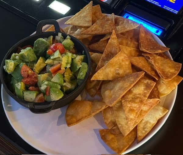 Crispy tortilla chips served with a bowl of fresh guacamole topped with diced tomatoes and onions