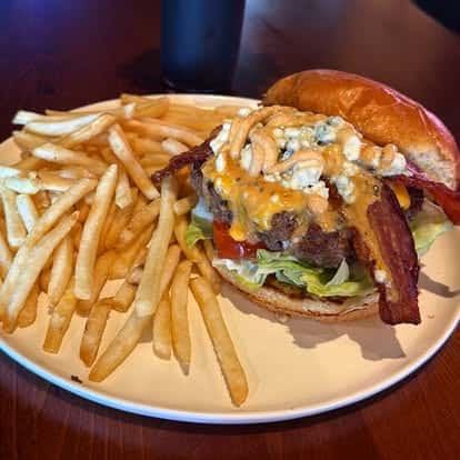 A bacon cheeseburger topped with blue cheese and sauce, served with thin-cut fries.