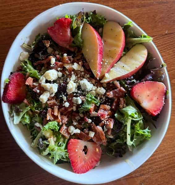 Fresh mixed green salad with sliced strawberries, apples, crumbled cheese, and candied pecans in a white bowl