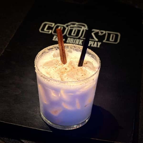 A creamy iced cocktail dusted with spice and garnished with a cinnamon stick on a Cook'd bar mat.