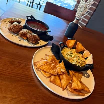 Tortilla chips with a hot, cheesy dip, alongside fried appetizers and a skillet of red dipping sauce.